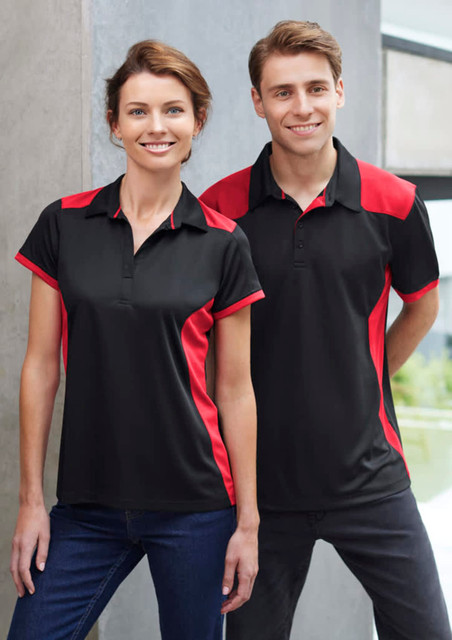 A black polo shirt with red accents, modelled by a man and a woman standing together indoors.