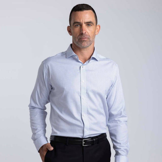 A men's button-up shirt in a blue and white check pattern with a collar and long sleeves. Features a logo.