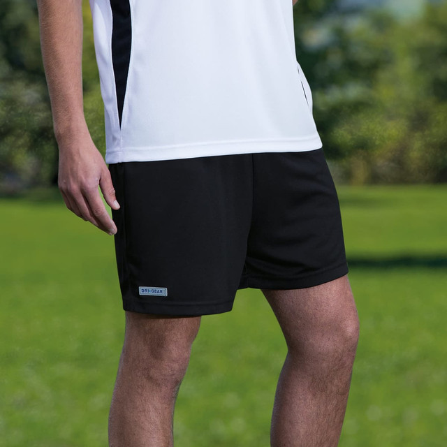 Dri Gear shorts in black, showcased alongside a white sports top, set against a green outdoor background. Dri Gear shorts in black, showcased alongside a white sports top, set against a green outdoor background.