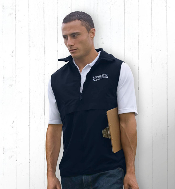 A man wearing a black nylon vest with a logo, holding a clipboard, standing against a white wooden background. A man wearing a black nylon vest with a logo, holding a clipboard, standing against a white wooden background.