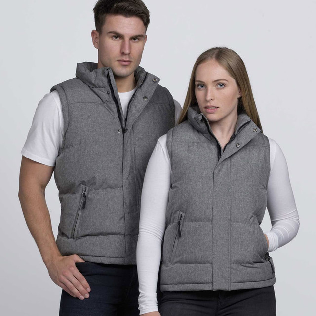 A grey puffer vest is worn by a man and a woman, both posing against a plain background. The vest has a logo. A grey puffer vest is worn by a man and a woman, both posing against a plain background. The vest has a logo.