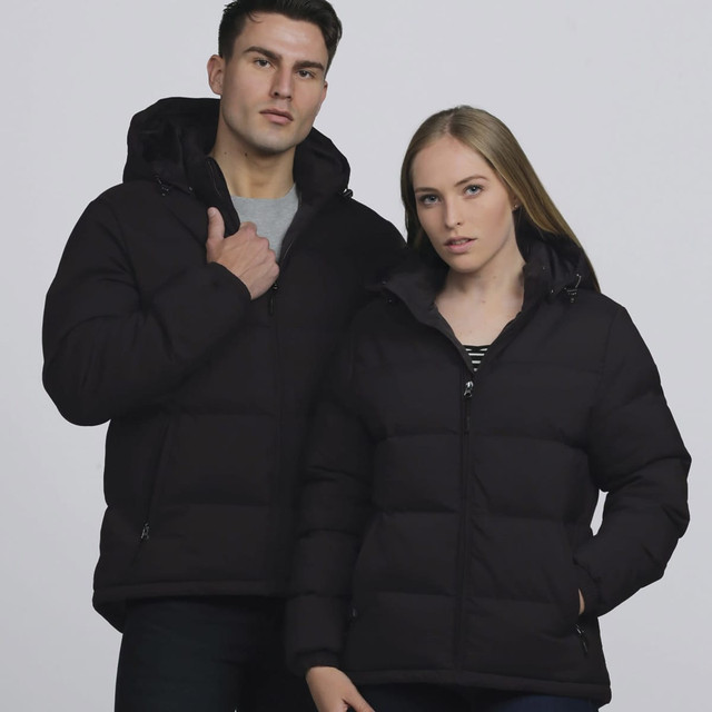 A black puffer jacket worn by a man and a woman, featuring hoods and a logo on the clothing. A black puffer jacket worn by a man and a woman, featuring hoods and a logo on the clothing.