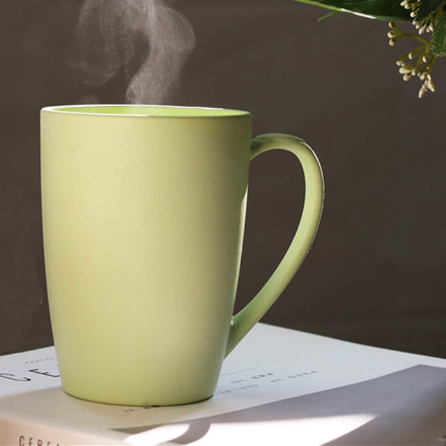 A green bamboo mug with a handle, emitting steam, resting on a white book.