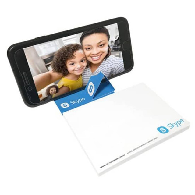 A phone holder in blue and white, supporting a smartphone, beside a notepad. The holder has a logo.