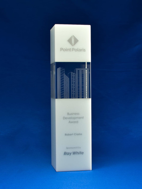 A crystal tower award in clear glass with a city skyline design, against a blue background. It features a logo and text. A crystal tower award in clear glass with a city skyline design, against a blue background. It features a logo and text.