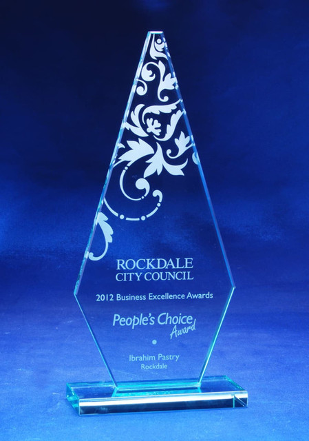 A jade glass arrowhead trophy with decorative etchings, featuring a clear base and set against a blue background. A jade glass arrowhead trophy with decorative etchings, featuring a clear base and set against a blue background.