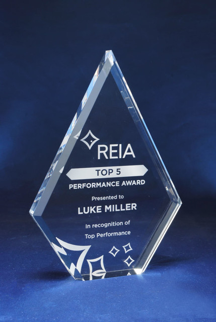 A diamond-shaped acrylic trophy with a clear finish and a blue background. Features engraving and a logo. A diamond-shaped acrylic trophy with a clear finish and a blue background. Features engraving and a logo.