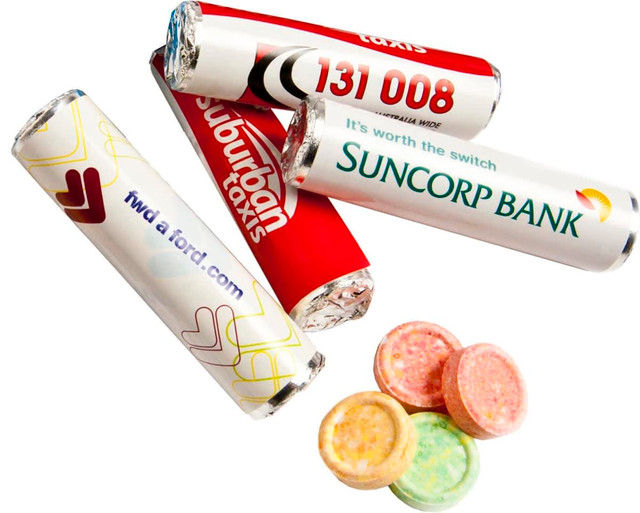 A selection of colourful round lollies beside multiple rolls of branded confectionery wrappers in red and white. A selection of colourful round lollies beside multiple rolls of branded confectionery wrappers in red and white.