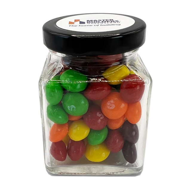 A small glass jar filled with colourful Skittles in various shades, topped with a black lid and featuring a logo. A small glass jar filled with colourful Skittles in various shades, topped with a black lid and featuring a logo.