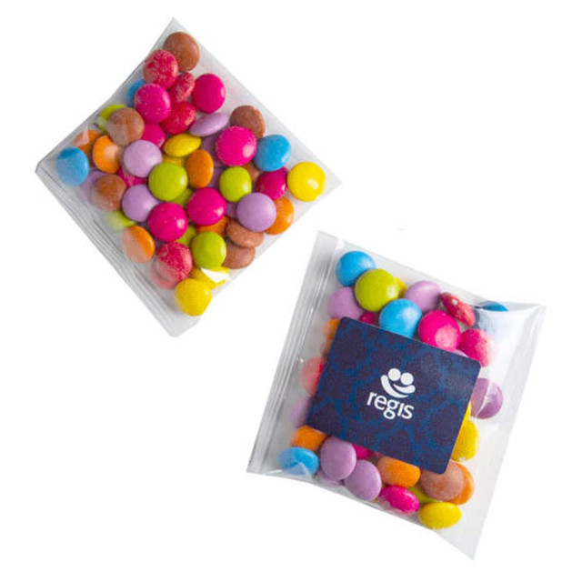 A clear bag containing colourful chocolate-coated candies in vibrant shades of pink, yellow, blue, and brown. The bag features a logo. A clear bag containing colourful chocolate-coated candies in vibrant shades of pink, yellow, blue, and brown. The bag features a logo.