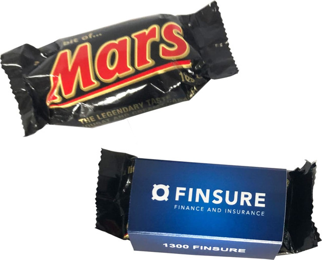 A Mars Bar wrapped in black packaging with bold red lettering, alongside a blue box featuring a logo. A Mars Bar wrapped in black packaging with bold red lettering, alongside a blue box featuring a logo.