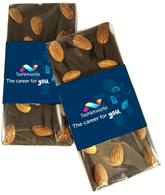 A chocolate bar with almonds arranged on top, wrapped in clear packaging featuring a logo and branding.
