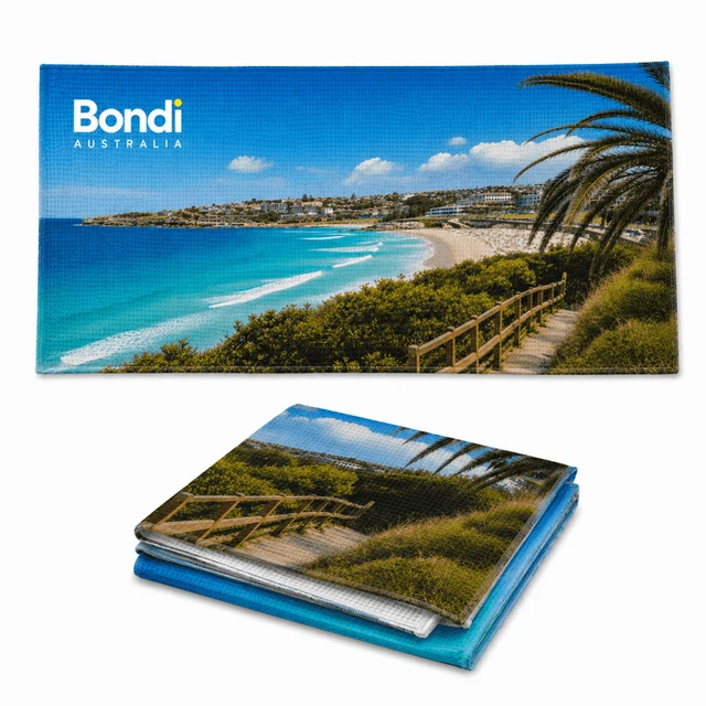 A sandless beach towel featuring a scenic Bondi Beach landscape with vibrant blue and green colours. It has a logo.