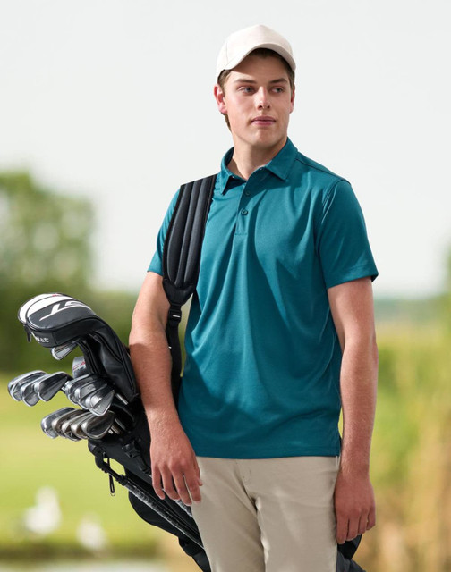 A man wearing a black short-sleeve polo shirt sits outdoors, holding a mug and smiling. The background is blurred.