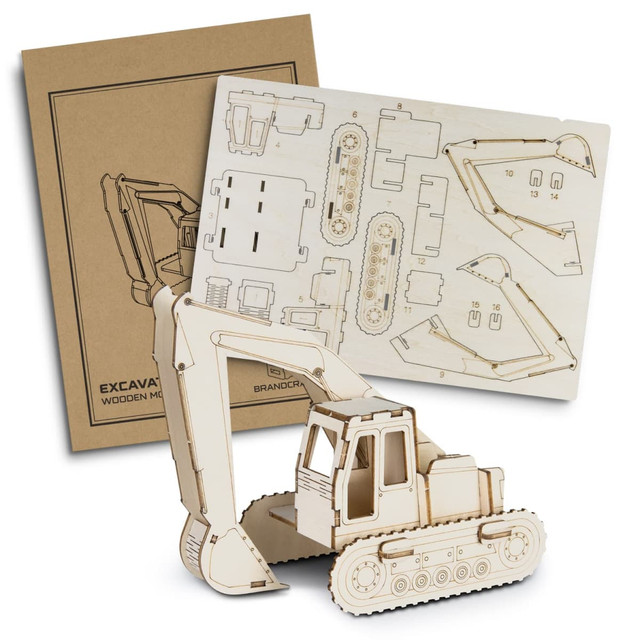 A wooden model of an excavator in a natural finish alongside its assembly instructions on a kraft background.