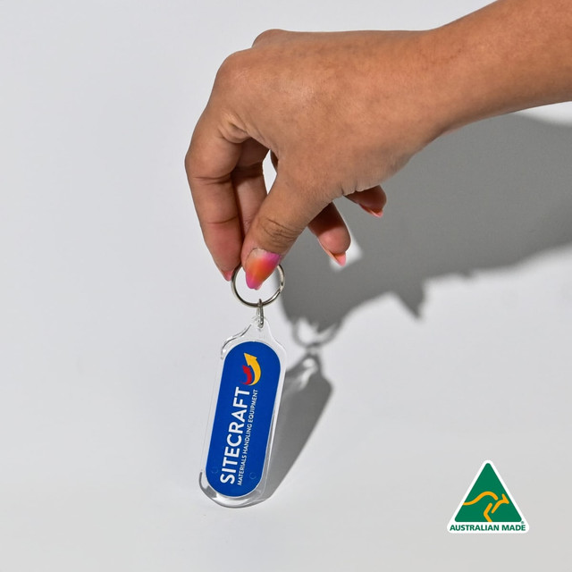An oval acrylic keychain in blue, held by a hand, featuring a logo and an Australian Made badge.