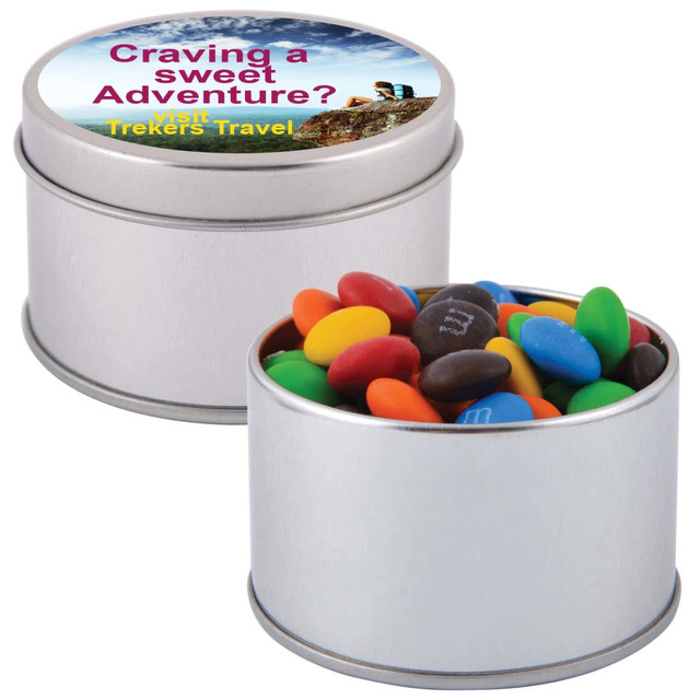 A silver round tin filled with colorful M&M's, featuring a lid with a design and a logo.