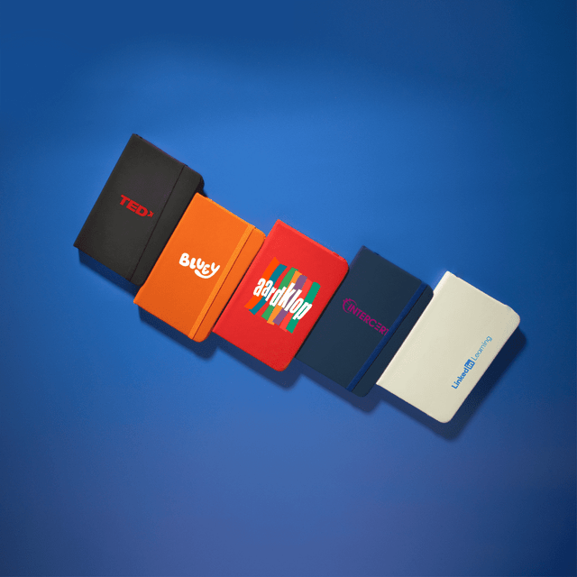 A collection of five Minichroma A6 Notebooks in various colours: red, orange, blue, navy, and white, each featuring a logo.