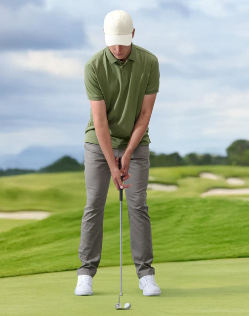 A golfer is putting on a green golf course, wearing a light-coloured cap, green polo shirt, and grey trousers.