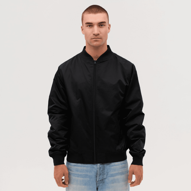 A black bomber jacket worn by a model, featuring a zip front and ribbed cuffs. The model has short hair and is standing against a neutral background.