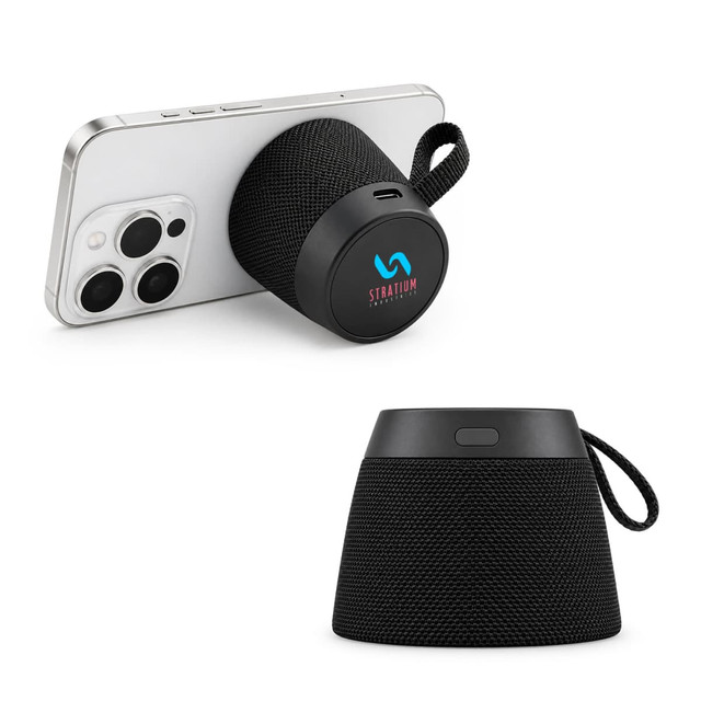 A black portable speaker with a fabric design, displayed with a phone leaning against it. Features a logo.