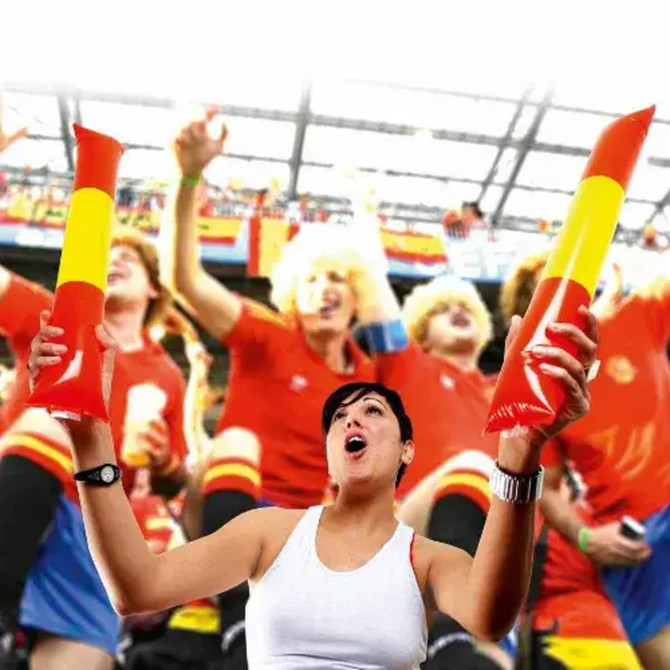 A woman holds red and yellow inflatable cheer sticks, surrounded by exuberant fans in a stadium.