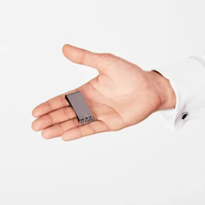 A sleek, grey money clip held in a hand, featuring a simple design and a logo on its surface.