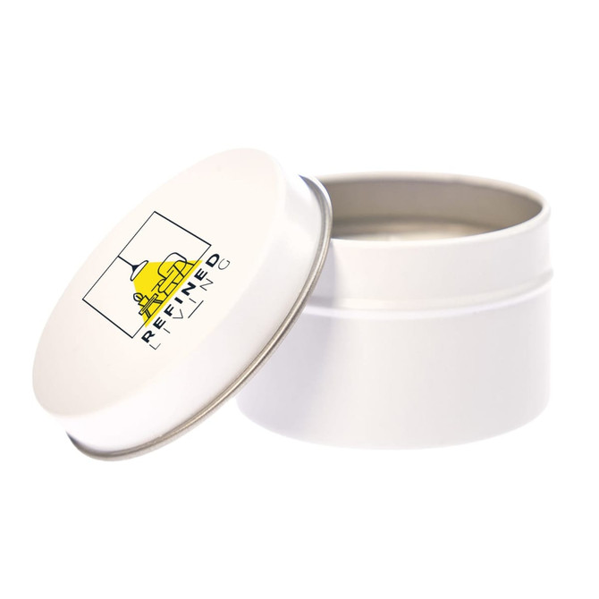 A white tin candle with a metal lid, featuring a logo on the top. The candle is unlit and inside the tin.