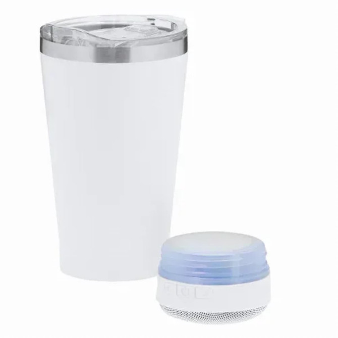 An insulated white cup with a silver rim beside a small blue speaker. Both items are positioned upright.