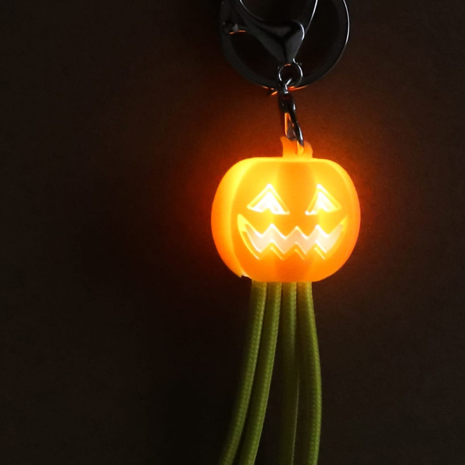 A bright orange pumpkin-shaped light with green charging cables, attached to a keyring, featuring a smiling face.