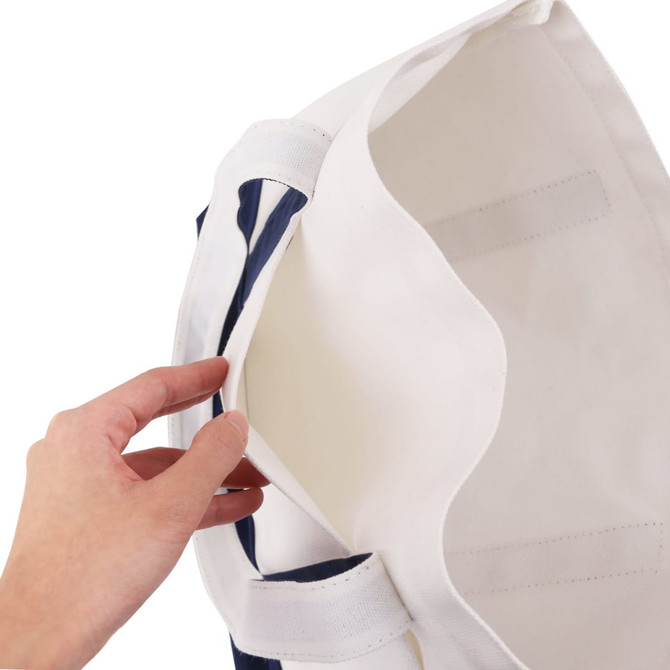 A hand reaches into a small canvas tote bag, featuring a navy blue exterior and a natural interior. The bag has a logo.