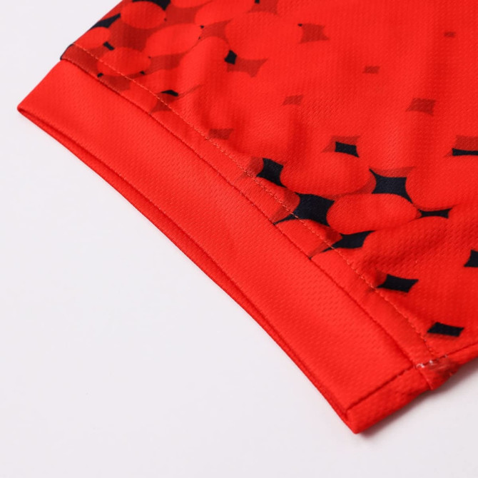 A close-up of a red football jersey featuring a patterned design and a logo. The fabric is 100% polyester.