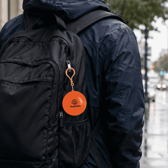 An orange rain poncho ball attached to a black backpack, showcasing a compact and portable design.