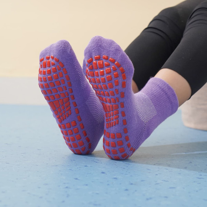 Purple gripper socks with red non-slip soles, designed for kids, displayed on a blue floor.