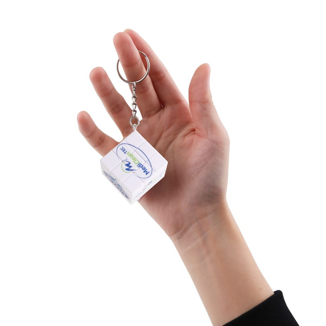 A hand holding a clear 3x3 puzzle cube keyring with a silver chain and ring attachment.