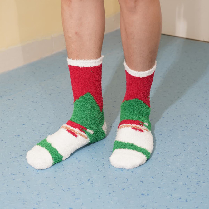 A pair of cosy socks featuring a red, green, and white design, worn on feet standing on a blue floor.