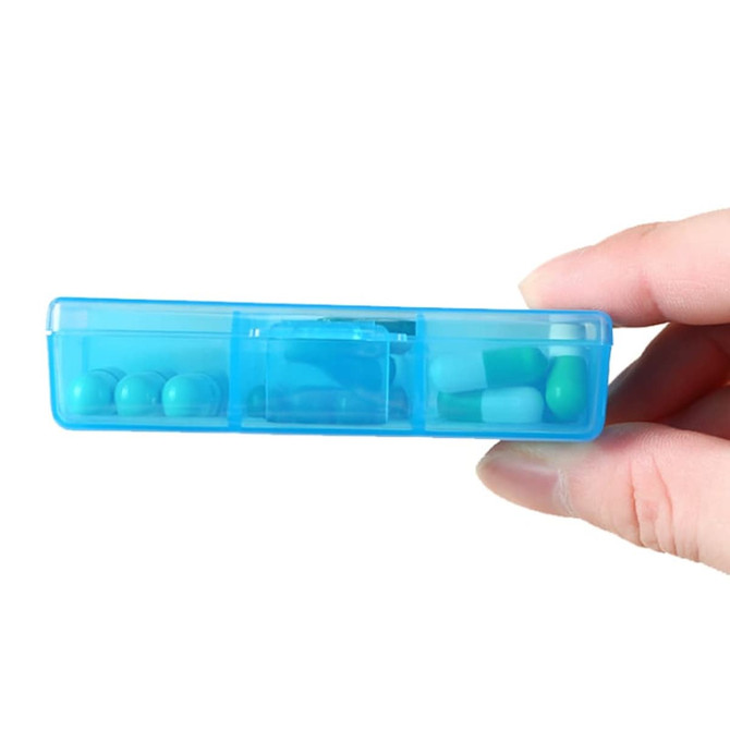 A blue square pill box with six compartments and various pills visible inside, held in a hand.