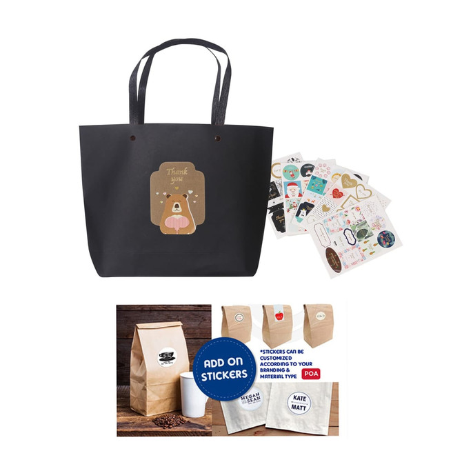 A black paper bag with handles, featuring a cute bear design, accompanied by assorted stickers.
