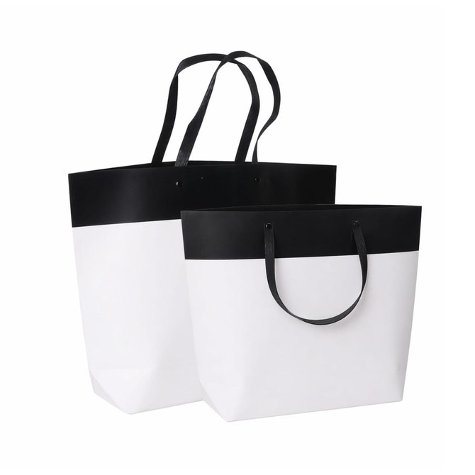 A small black and white paper bag with a black top and white bottom, featuring sturdy handles.
