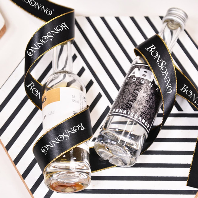 A pair of glass bottles wrapped in a black ribbon with gold edges and a branding logo. The background features a striped design.