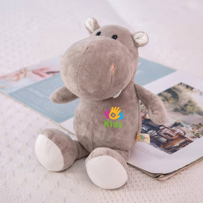 A soft grey hippopotamus plush toy with embroidered details and a small logo, sitting on a textured surface.