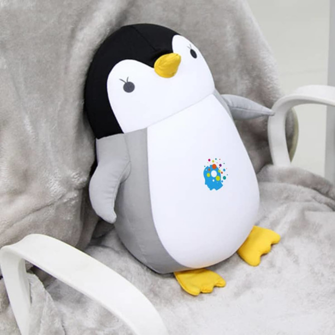 A penguin-shaped plush travel pillow in black, white, and yellow, featuring a small logo on its belly.