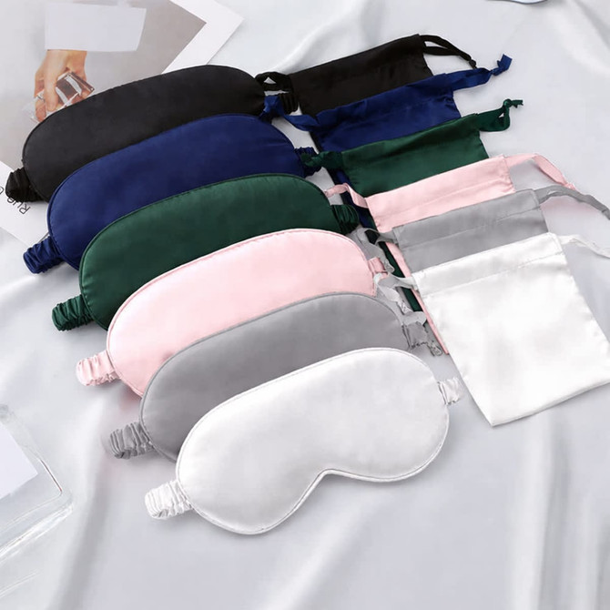 A collection of satin sleep masks in various colours, including navy, green, pink, grey, and white, with packaging.