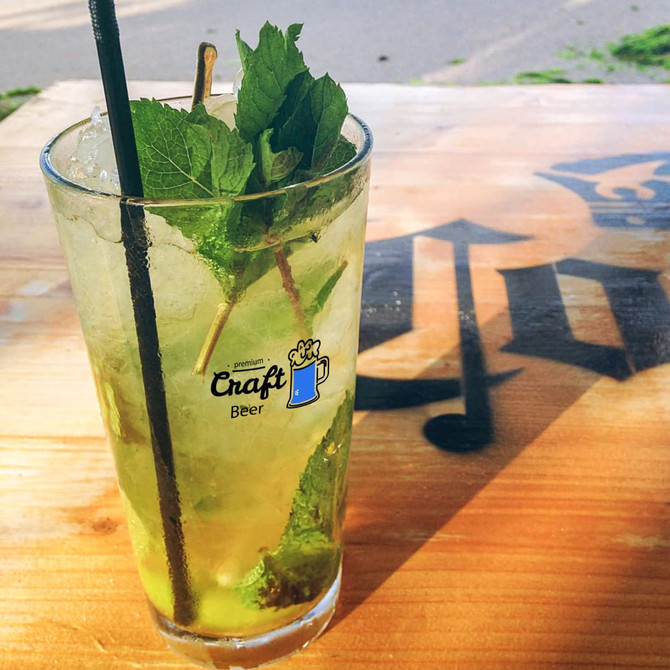 A tall glass tumbler filled with a minty green drink, garnished with fresh mint leaves and a straw.