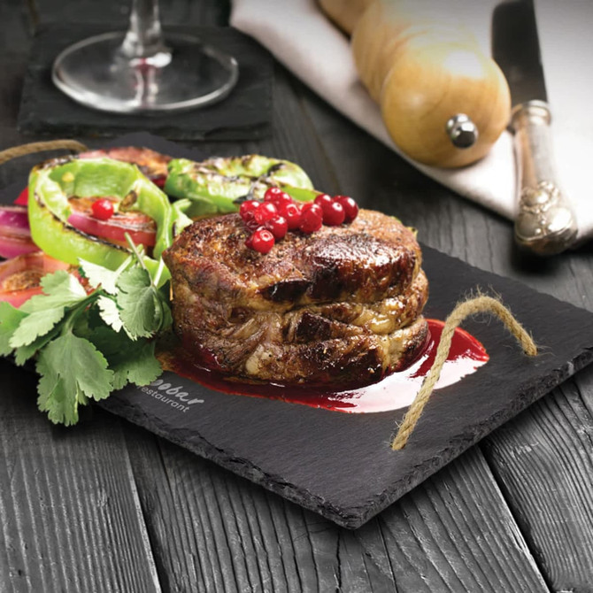 A slate serving board with grilled meat, vegetables, and garnishes, featuring a rustic string handle.