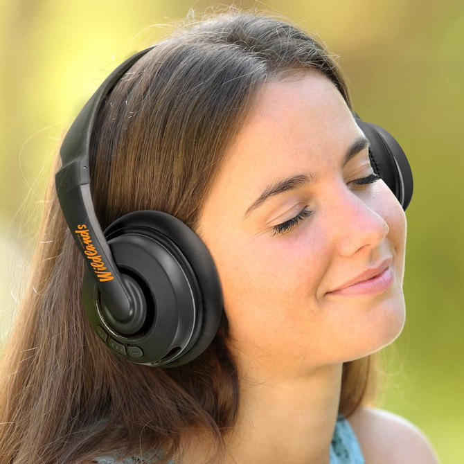 Black Skullcandy Cassette Headphones worn by a woman, featuring an orange logo, with a soft outdoor background.