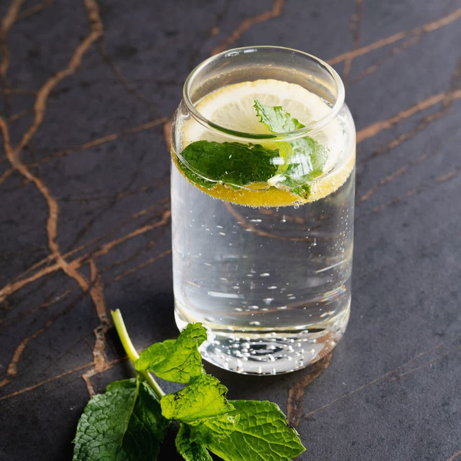 A clear glass filled with sparkling water, lemon slices, and fresh mint leaves, sitting on a dark marble surface.