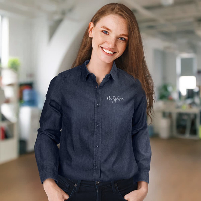 A woman wearing a navy denim button-up shirt with a logo on the chest, set in an office environment.