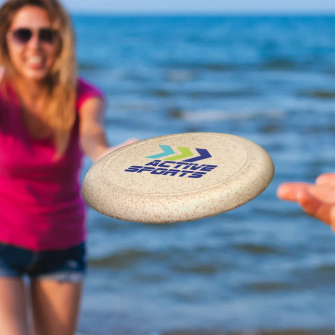 A frisbee in sandy beige, featuring a logo, being tossed by a person near water.