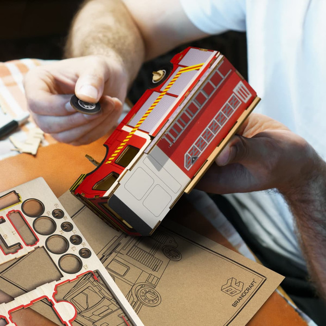 A red and white wooden model of a fire truck, with assembly parts and tools beside it.